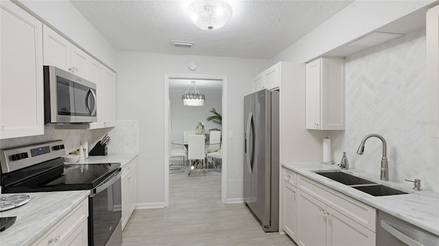 kitchen with white cabinets, appliances with stainless steel finishes, light stone countertops, and sink