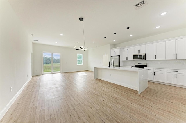 kitchen with appliances with stainless steel finishes, a kitchen island with sink, white cabinets, light hardwood / wood-style floors, and hanging light fixtures