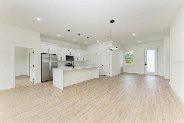 kitchen with hanging light fixtures, light hardwood / wood-style floors, a kitchen island with sink, white cabinets, and appliances with stainless steel finishes