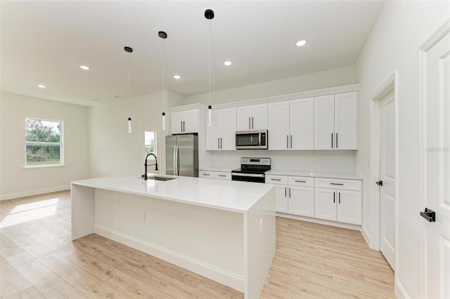 kitchen featuring white cabinets, appliances with stainless steel finishes, a kitchen island with sink, and pendant lighting