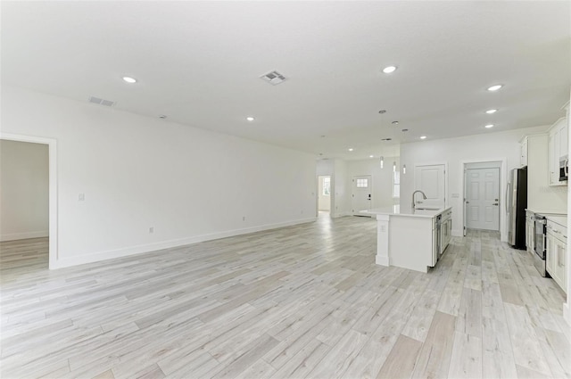 kitchen with white cabinetry, sink, stainless steel appliances, a kitchen island with sink, and light wood-type flooring