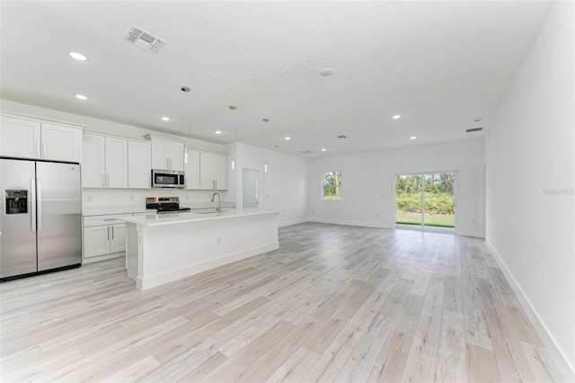 kitchen with white cabinets, a center island with sink, light wood-type flooring, decorative light fixtures, and stainless steel appliances