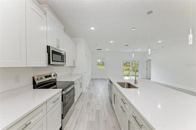 kitchen featuring pendant lighting, white cabinets, sink, appliances with stainless steel finishes, and light stone counters