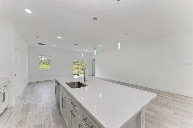 kitchen featuring a center island with sink, sink, light wood-type flooring, light stone countertops, and decorative light fixtures