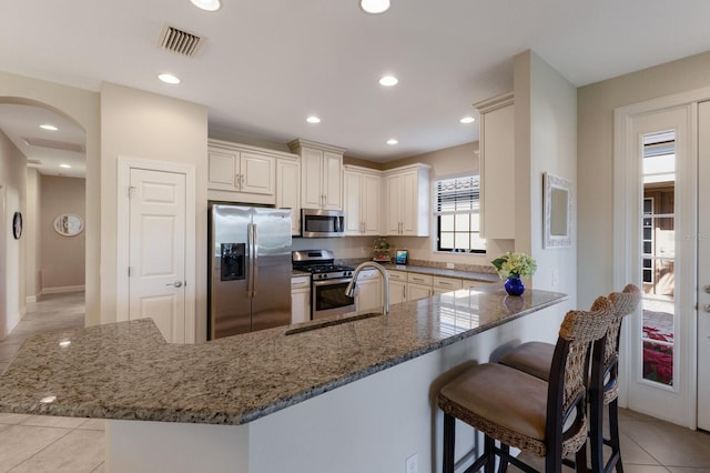 kitchen with a kitchen bar, stainless steel appliances, dark stone counters, kitchen peninsula, and light tile patterned flooring