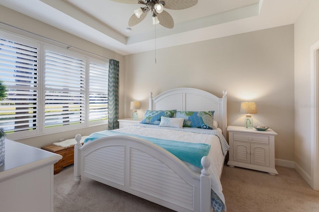 carpeted bedroom with ceiling fan and a raised ceiling