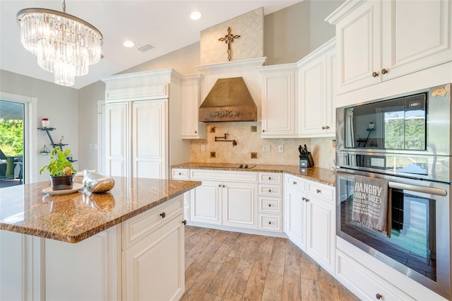 kitchen with premium range hood, white cabinets, a kitchen island, and an inviting chandelier