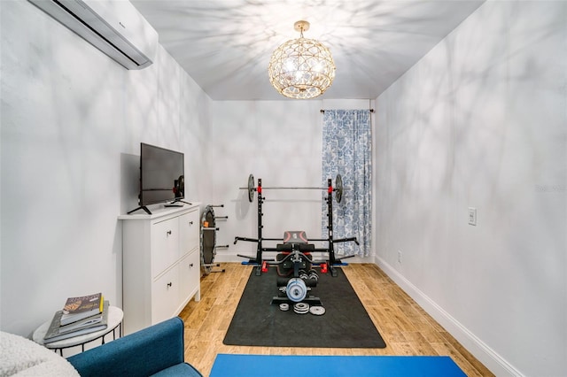 exercise room featuring light hardwood / wood-style floors, a wall mounted AC, and a notable chandelier