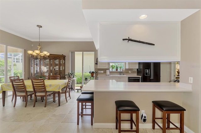 kitchen with black refrigerator with ice dispenser, an inviting chandelier, a kitchen breakfast bar, kitchen peninsula, and white cabinetry