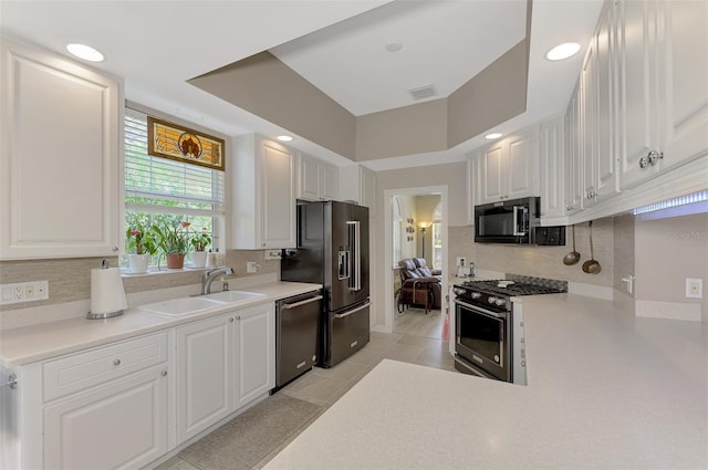 kitchen with white cabinets, sink, light tile patterned floors, a tray ceiling, and stainless steel appliances