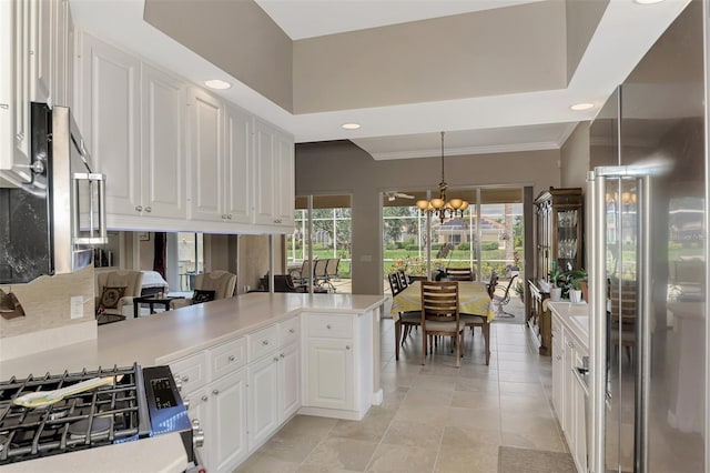 kitchen with white cabinetry, an inviting chandelier, high end refrigerator, kitchen peninsula, and pendant lighting