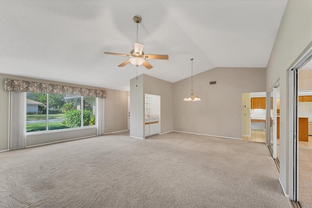 unfurnished living room featuring ceiling fan with notable chandelier, light colored carpet, and vaulted ceiling