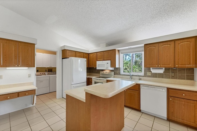 kitchen featuring white appliances, vaulted ceiling, sink, washing machine and clothes dryer, and a kitchen island