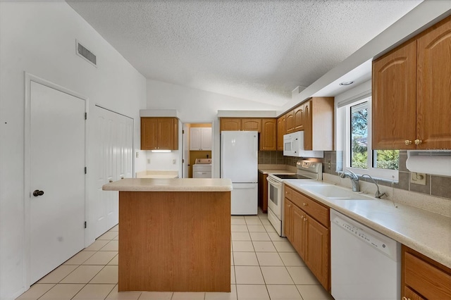 kitchen featuring lofted ceiling, white appliances, sink, a kitchen island, and washer / dryer