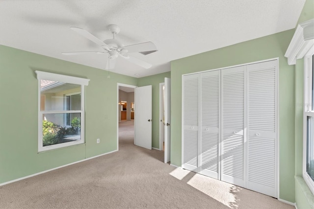 unfurnished bedroom featuring ceiling fan, multiple windows, light carpet, and a closet