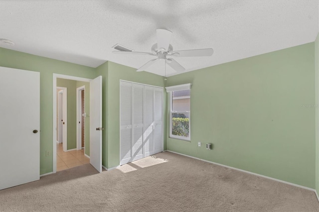 unfurnished bedroom featuring ceiling fan, light colored carpet, a textured ceiling, and a closet