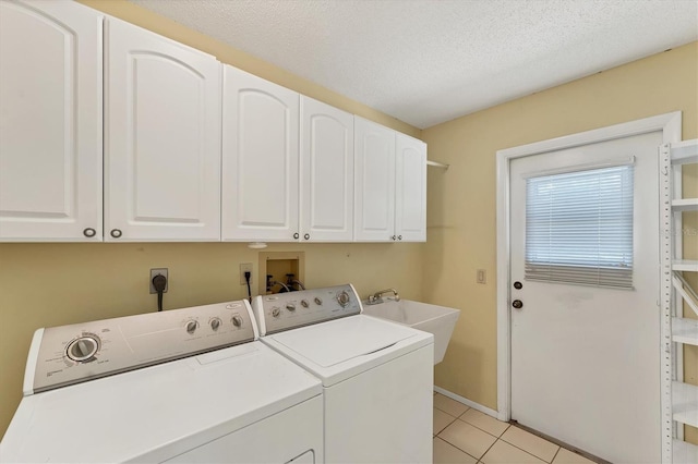 clothes washing area featuring cabinets, a textured ceiling, washer and clothes dryer, sink, and light tile patterned flooring