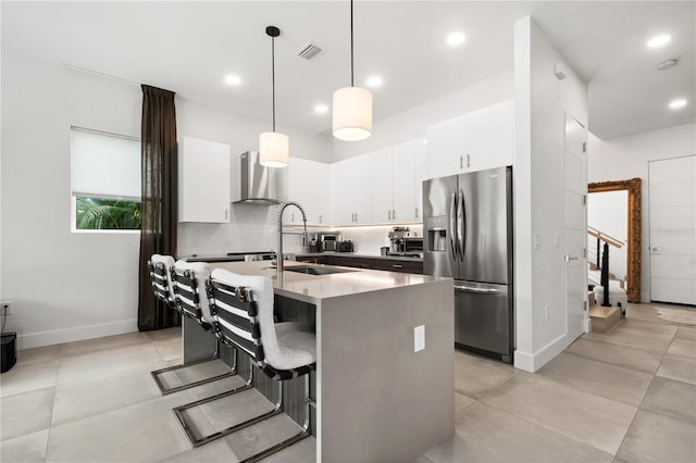 kitchen with stainless steel fridge, wall chimney exhaust hood, sink, pendant lighting, and a center island with sink