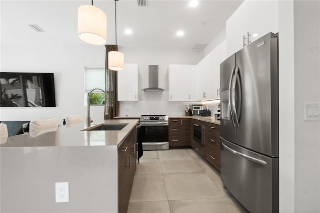 kitchen with sink, wall chimney exhaust hood, pendant lighting, white cabinets, and appliances with stainless steel finishes