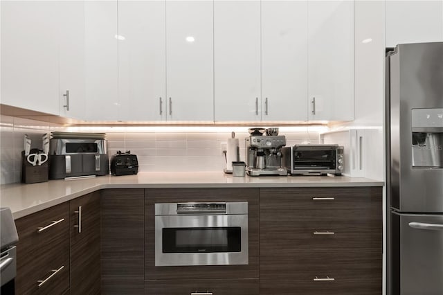 kitchen with white cabinets, decorative backsplash, dark brown cabinetry, and stainless steel appliances