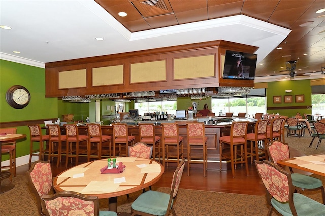 dining space with bar, ceiling fan, dark wood-type flooring, and ornamental molding