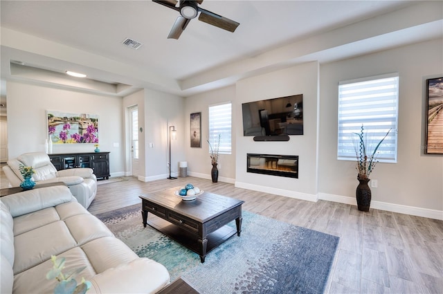 living room with hardwood / wood-style floors, ceiling fan, a healthy amount of sunlight, and a tray ceiling