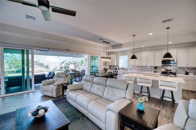 living room featuring ceiling fan, dark hardwood / wood-style flooring, sink, and a tray ceiling