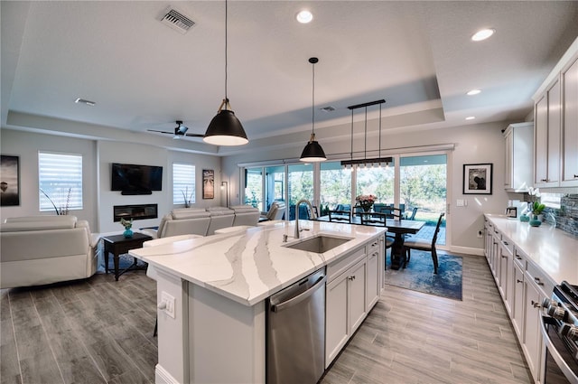 kitchen with a center island with sink, white cabinets, a raised ceiling, sink, and appliances with stainless steel finishes