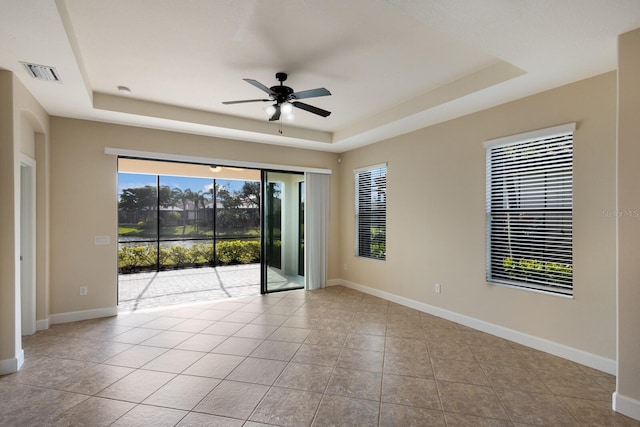 tiled spare room featuring ceiling fan and a tray ceiling