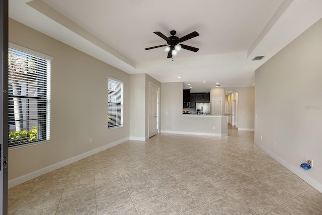 unfurnished living room featuring a raised ceiling, light tile patterned flooring, ceiling fan, and a wealth of natural light