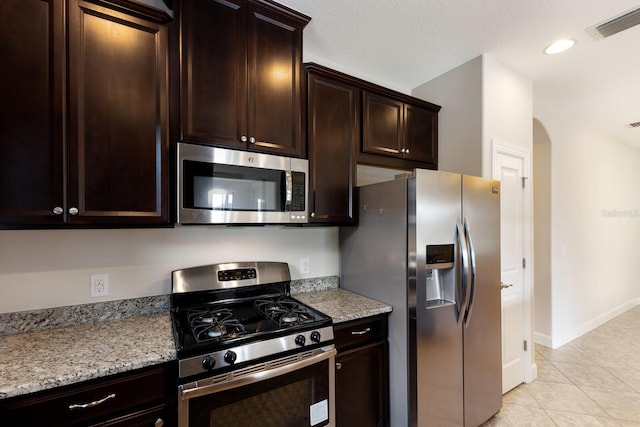 kitchen featuring light stone counters, appliances with stainless steel finishes, light tile patterned floors, and dark brown cabinets