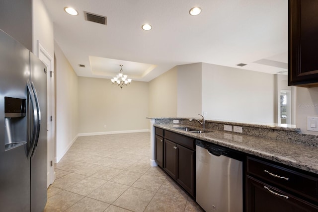 kitchen with an inviting chandelier, a raised ceiling, stainless steel appliances, sink, and stone countertops