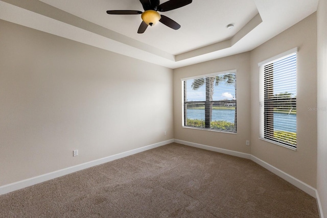 spare room featuring ceiling fan, carpet floors, a tray ceiling, and a water view