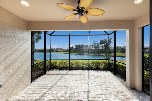 unfurnished sunroom featuring ceiling fan and a water view