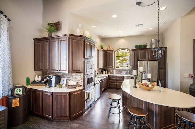 kitchen featuring stainless steel appliances, dark brown cabinets, dark hardwood / wood-style flooring, and backsplash