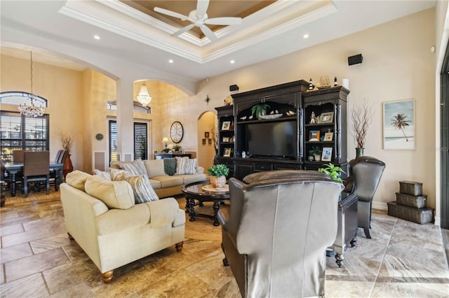 living room with a raised ceiling, crown molding, a towering ceiling, and ceiling fan with notable chandelier