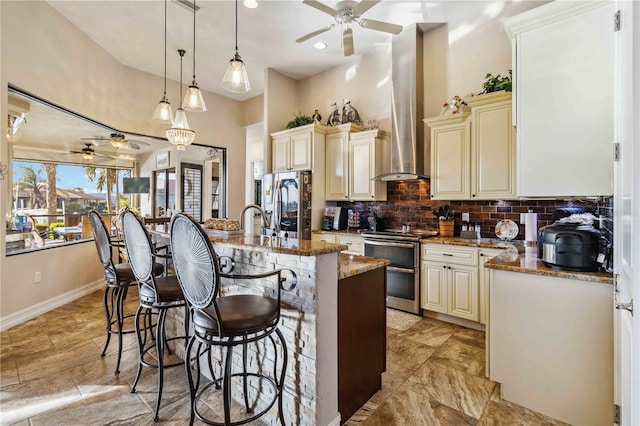 kitchen with appliances with stainless steel finishes, light stone counters, pendant lighting, cream cabinets, and an island with sink