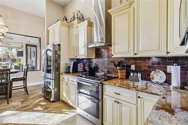 kitchen with wall chimney exhaust hood, stone countertops, cream cabinetry, decorative backsplash, and appliances with stainless steel finishes