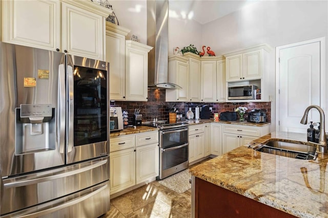 kitchen featuring cream cabinets, sink, wall chimney exhaust hood, appliances with stainless steel finishes, and light stone counters