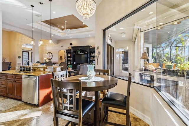 kitchen featuring light stone counters, a tray ceiling, sink, decorative light fixtures, and dishwasher