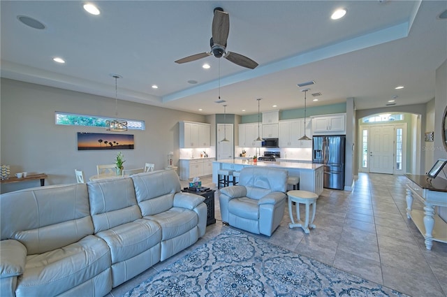 living room featuring light tile patterned floors, a tray ceiling, and ceiling fan