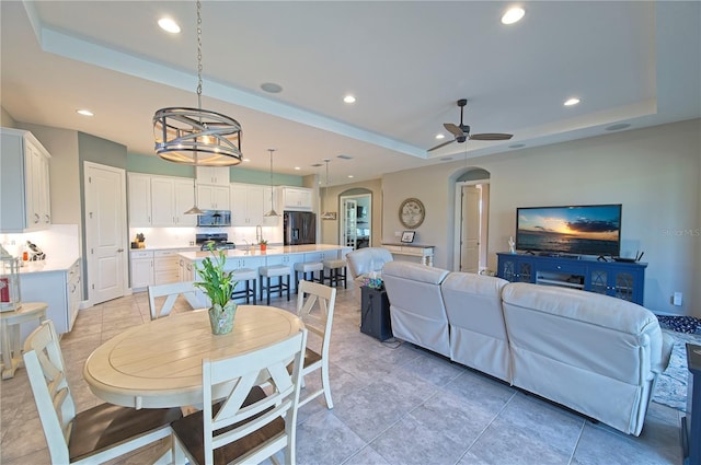 dining area with a raised ceiling, ceiling fan, and light tile patterned floors