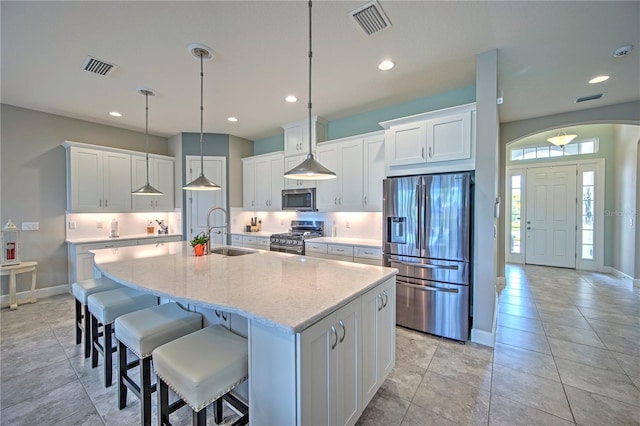 kitchen featuring white cabinets, hanging light fixtures, sink, an island with sink, and appliances with stainless steel finishes