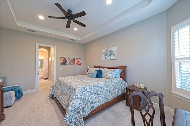 bedroom featuring ceiling fan, light colored carpet, ensuite bathroom, and a tray ceiling