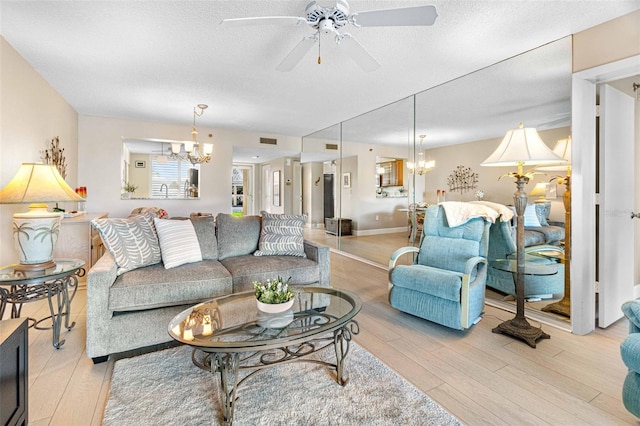 living room featuring ceiling fan with notable chandelier, a textured ceiling, and light hardwood / wood-style flooring