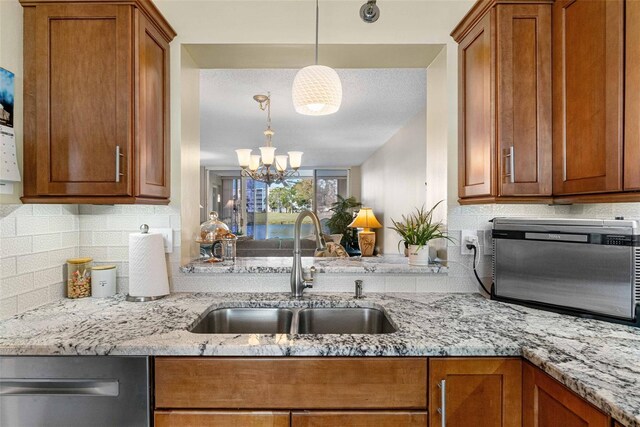 kitchen featuring light stone countertops, a notable chandelier, pendant lighting, sink, and stainless steel dishwasher