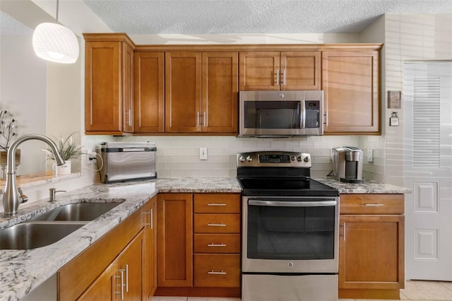 kitchen featuring light stone countertops, a textured ceiling, hanging light fixtures, appliances with stainless steel finishes, and sink