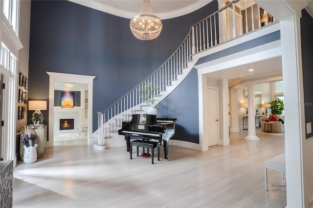 foyer with ornate columns, hardwood / wood-style floors, a high ceiling, crown molding, and an inviting chandelier