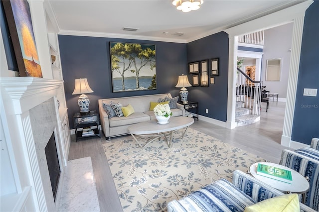 living room with a high end fireplace, ornamental molding, and light hardwood / wood-style floors