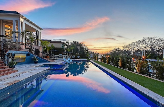 pool at dusk with an in ground hot tub and a patio area